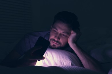 Photo of Man using smartphone in bed at night. Internet addiction