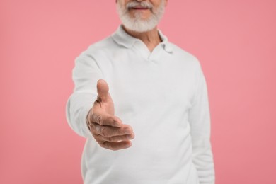 Man welcoming and offering handshake on pink background, closeup