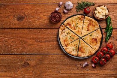 Photo of Delicious khachapuri with cheese, sauce and vegetables on wooden table, flat lay. Space for text