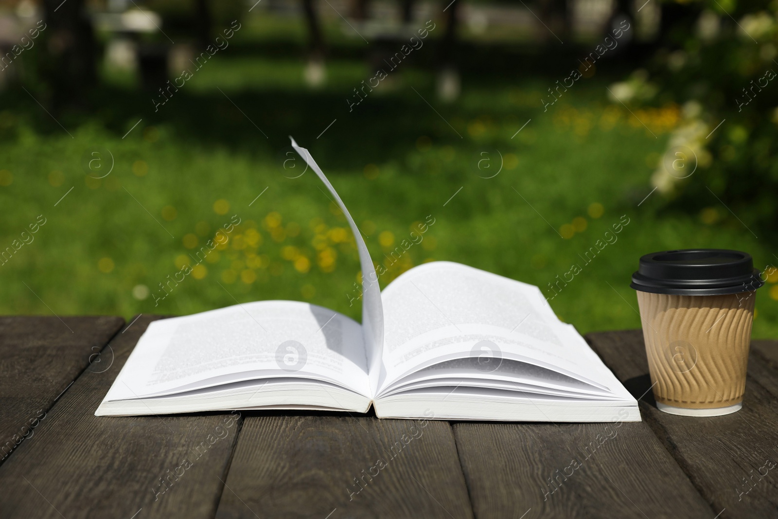 Photo of Open book and paper coffee cup on wooden table outdoors