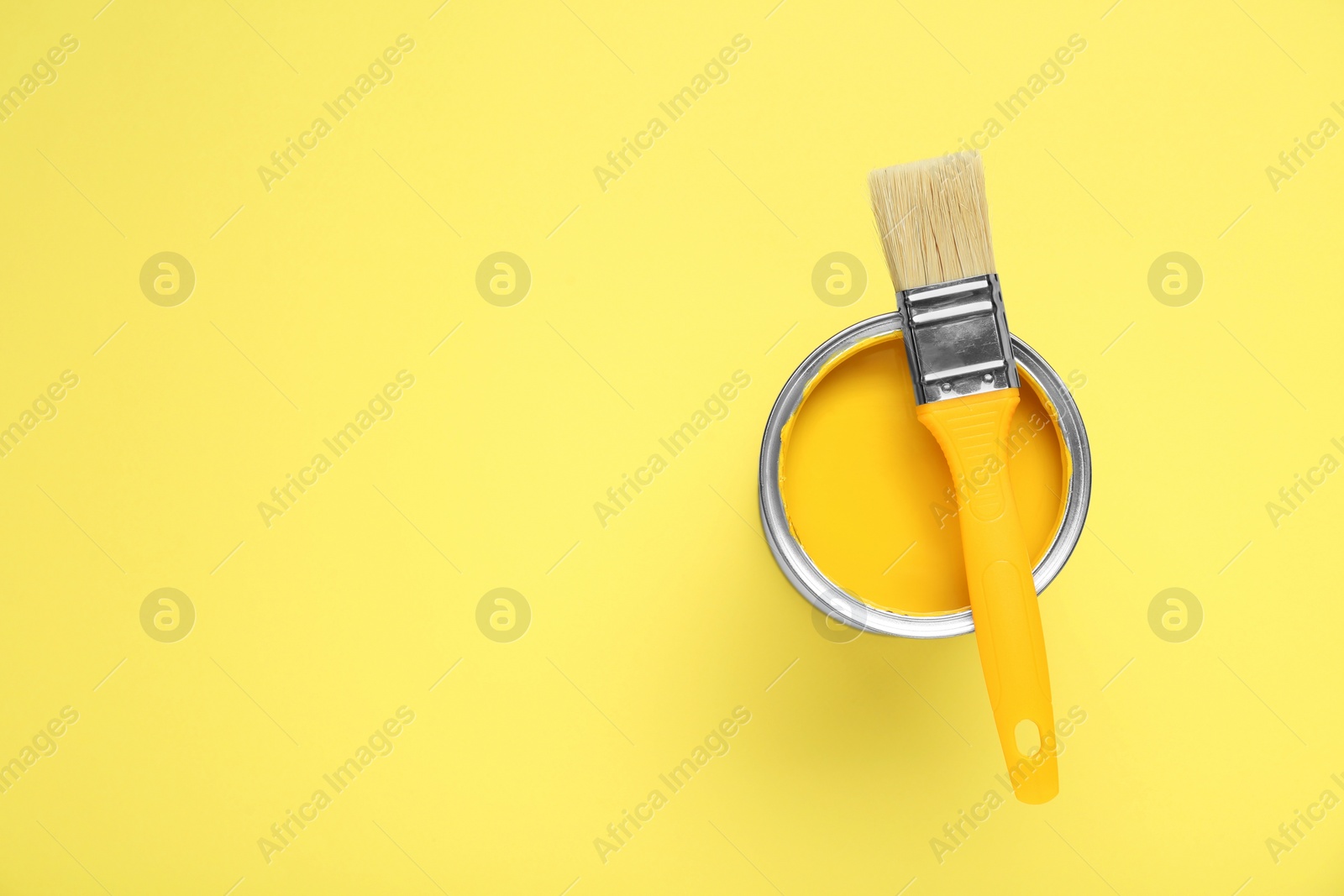 Photo of Can of paint with brush on pale yellow background, top view. Space for text