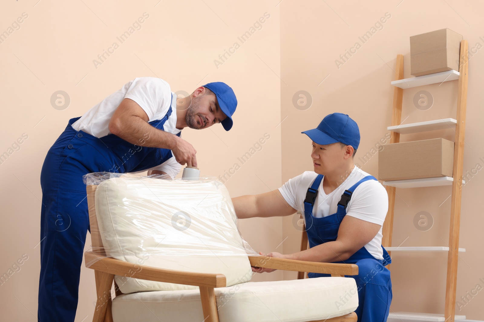 Photo of Workers wrapping armchair in stretch film indoors