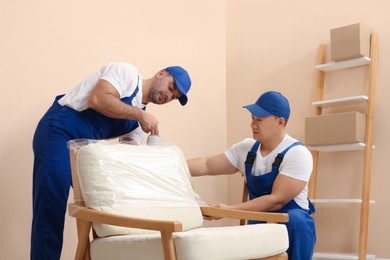 Photo of Workers wrapping armchair in stretch film indoors