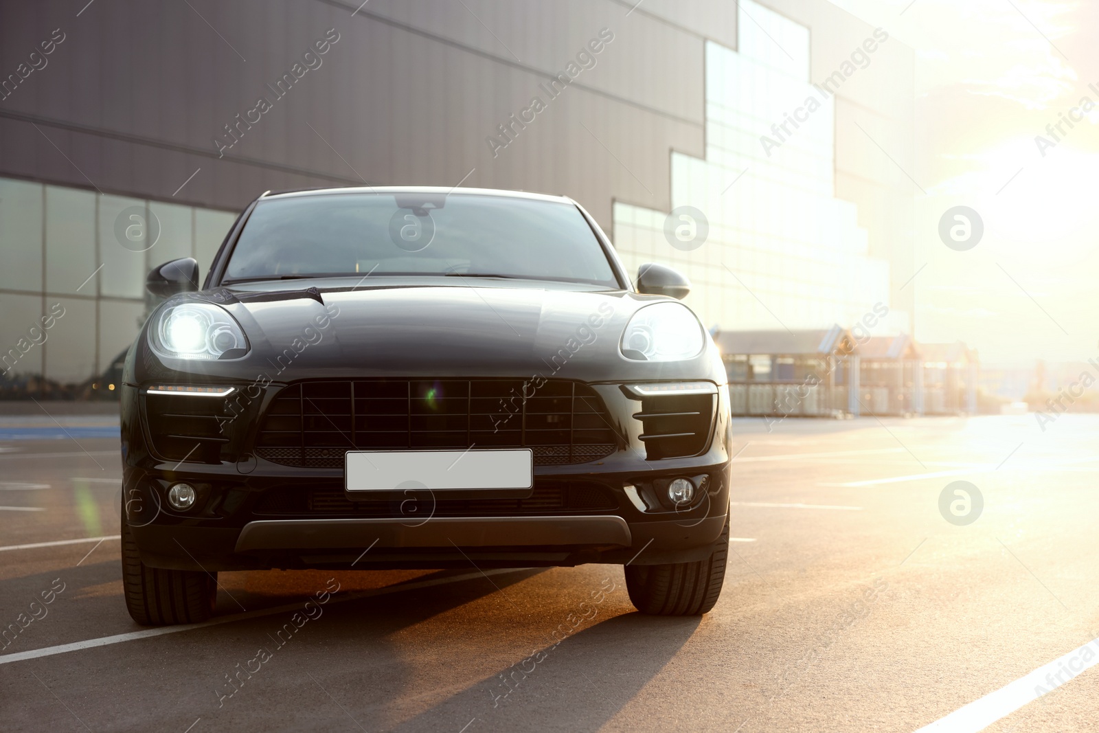 Photo of Modern black car parked on parking lot outdoors at sunrise