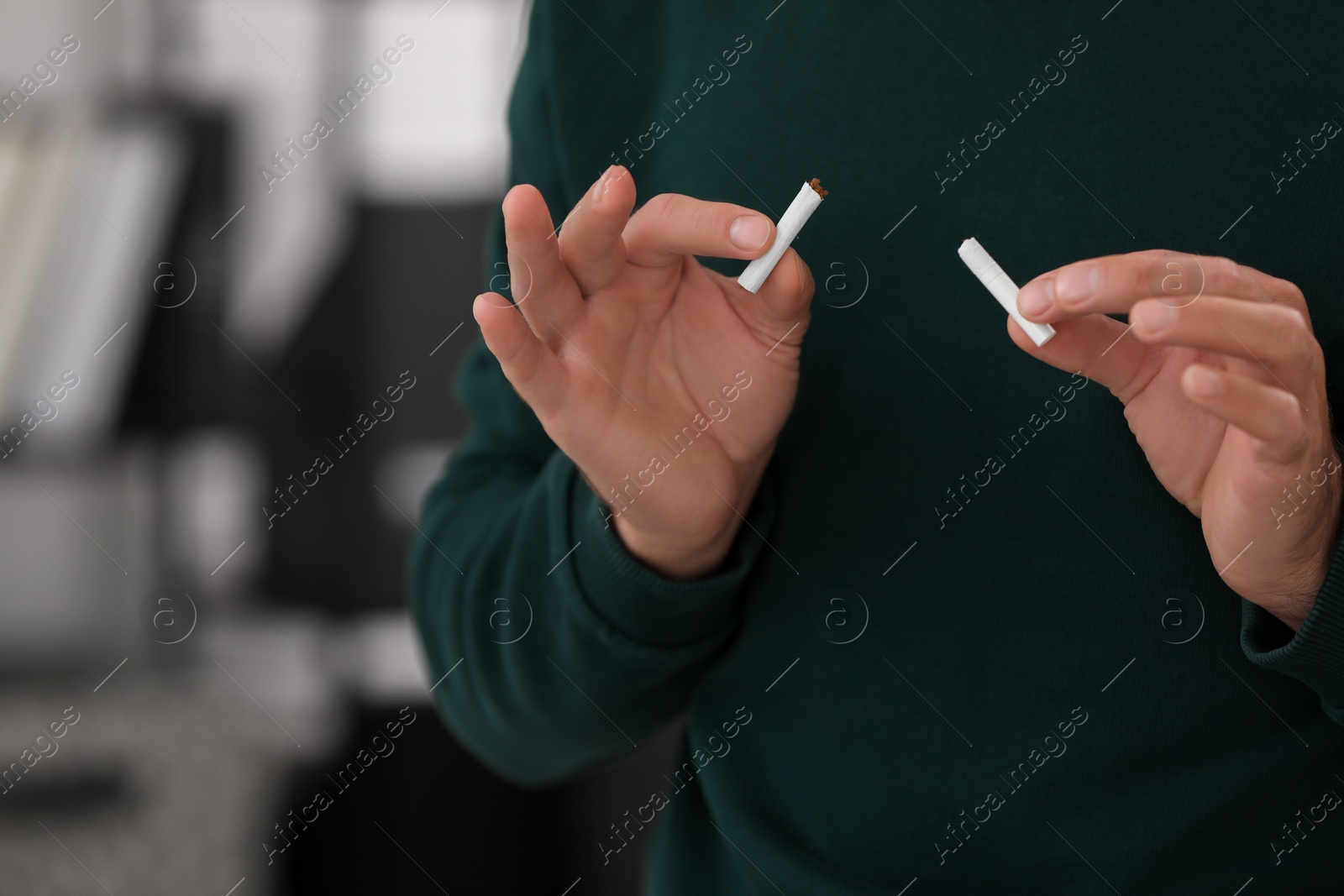 Photo of Stop smoking concept. Man holding pieces of broken cigarette on blurred background, closeup