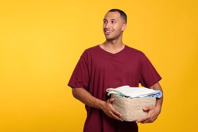 Happy man with basket full of laundry on orange background. Space for text