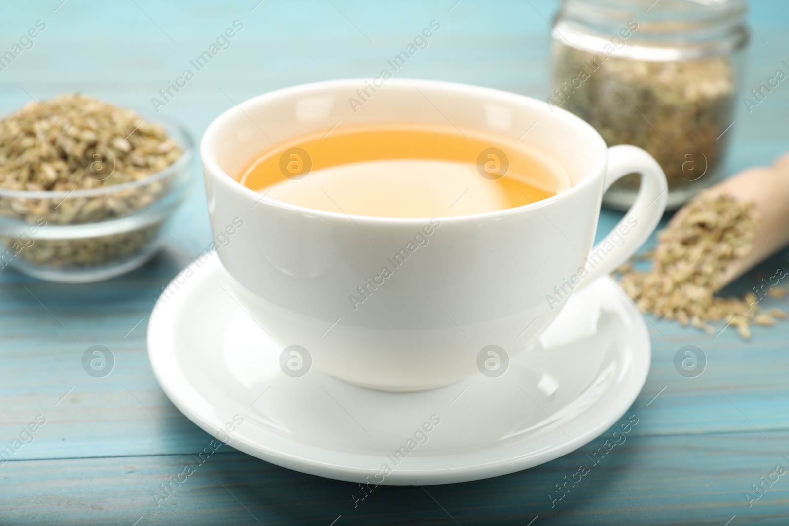 Photo of Fennel tea in cup and seeds on light blue wooden table, closeup