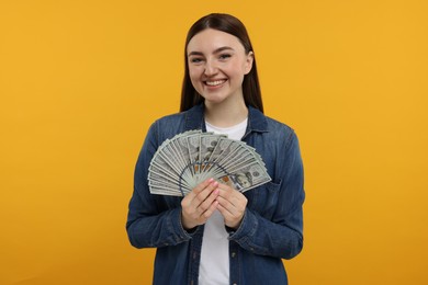 Photo of Happy woman with dollar banknotes on orange background