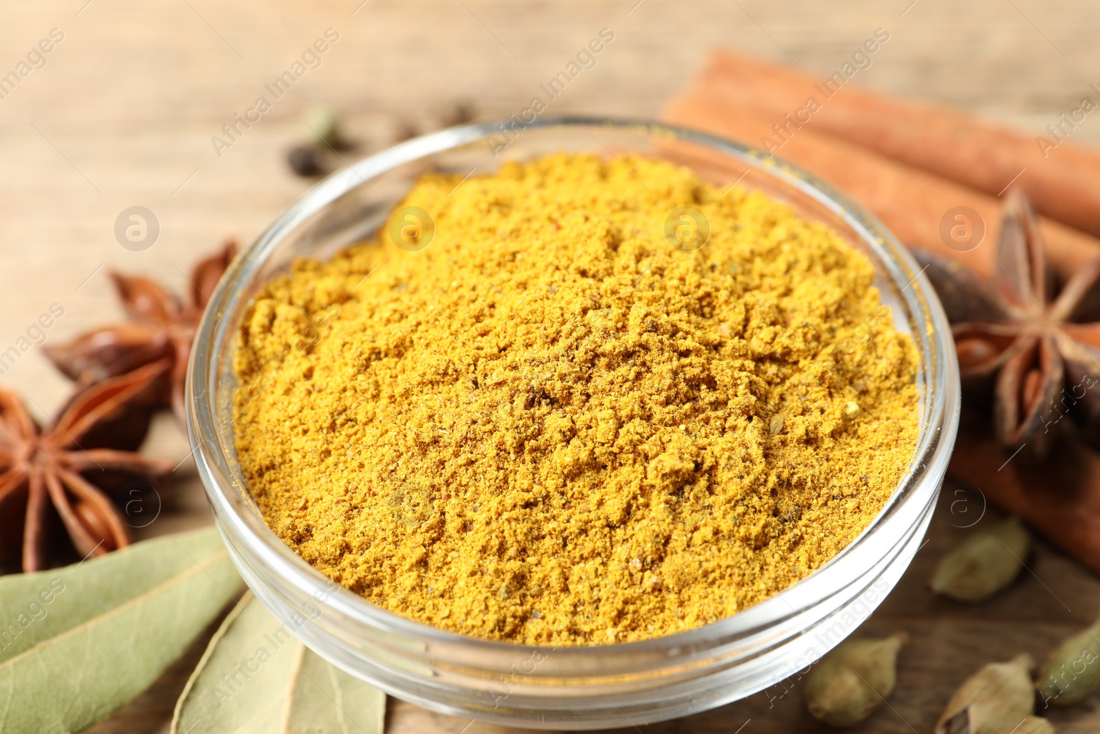 Photo of Curry powder in bowl and other spices on wooden table, closeup