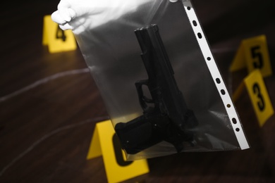 Photo of Detective holding plastic bag with gun at crime scene, closeup