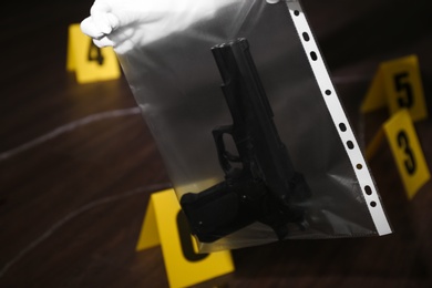 Detective holding plastic bag with gun at crime scene, closeup