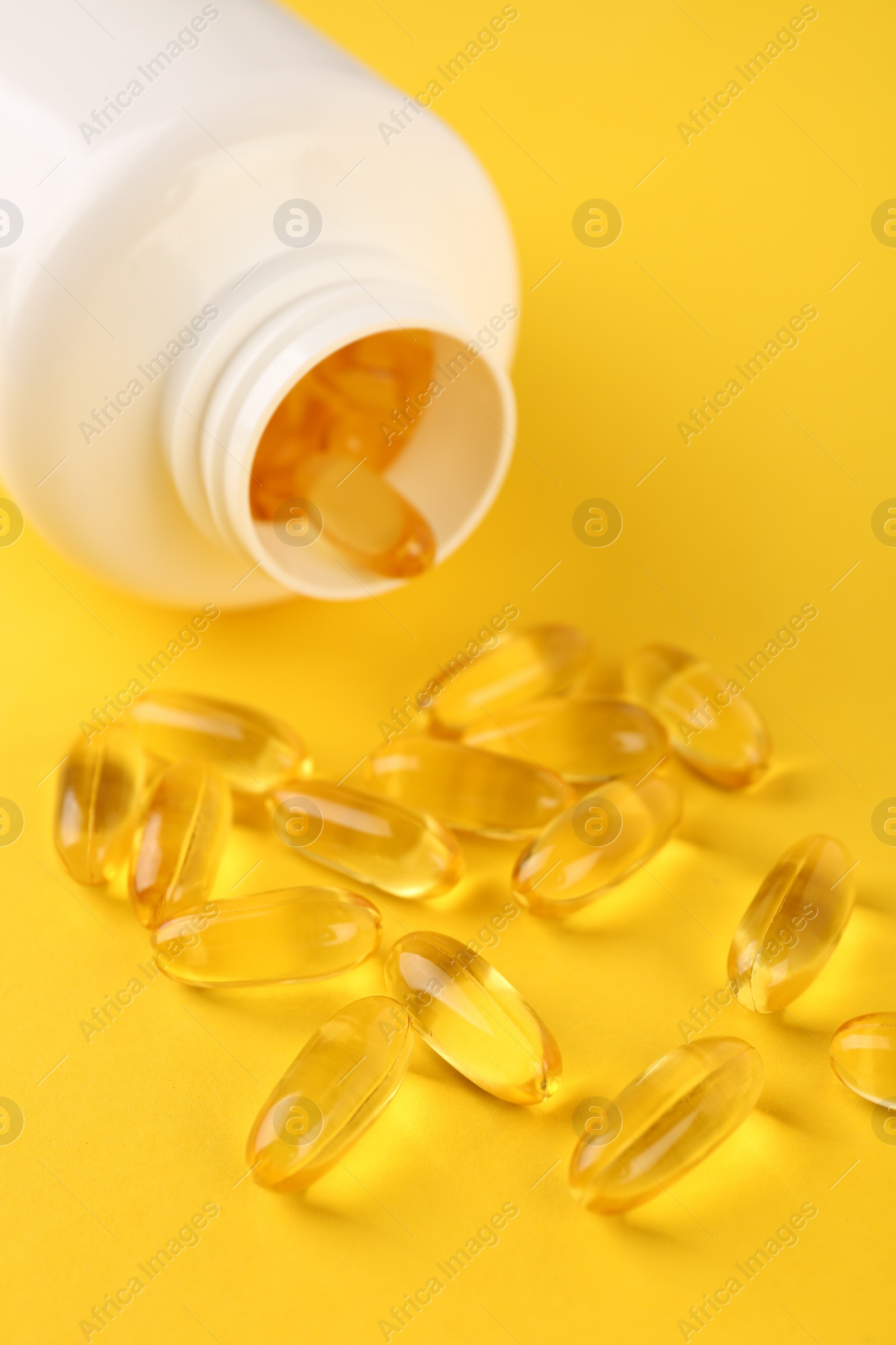 Photo of Vitamin capsules and medical bottle on yellow background, closeup