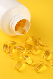 Photo of Vitamin capsules and medical bottle on yellow background, closeup