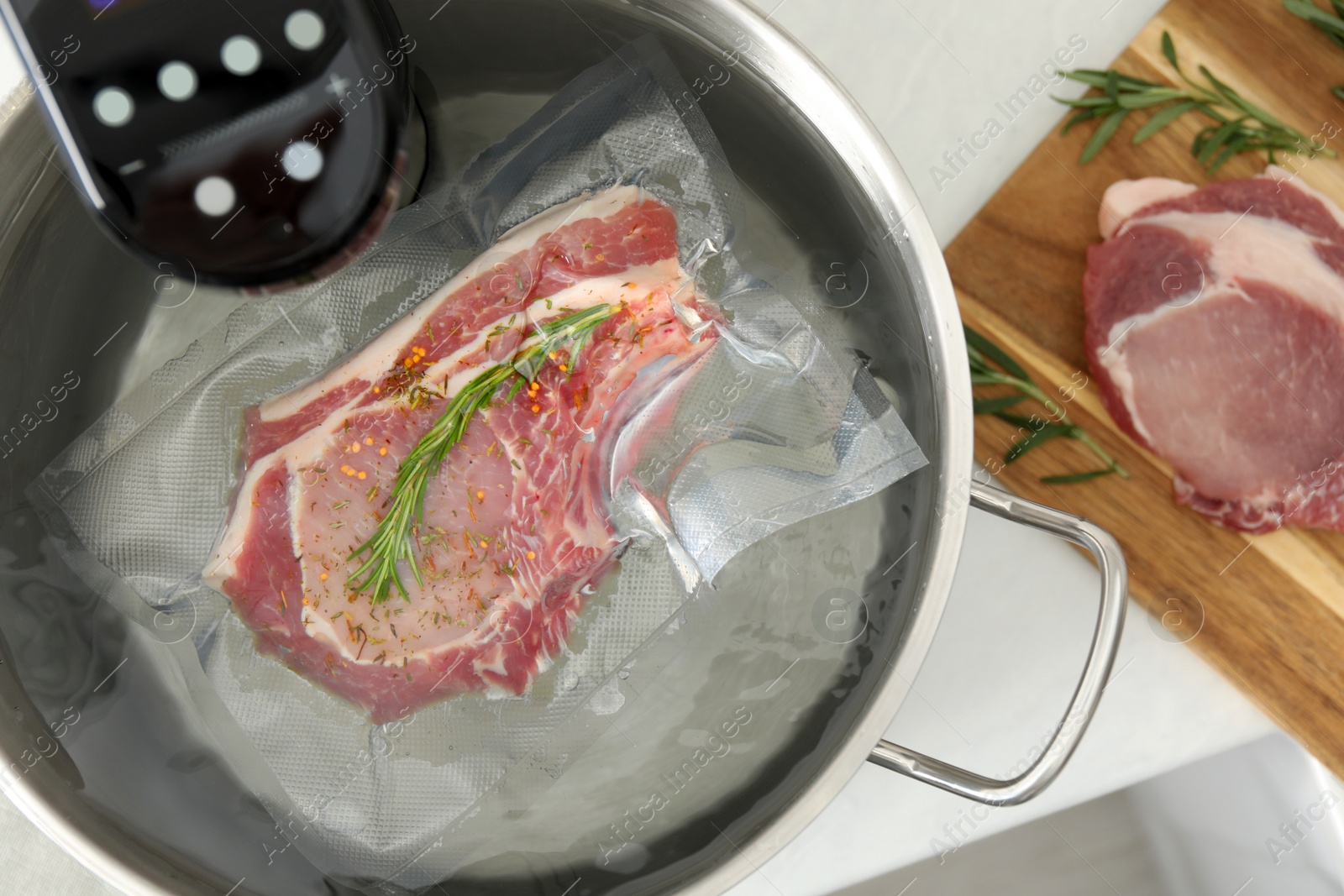 Photo of Sous vide cooker and vacuum packed meat in pot on white table, top view. Thermal immersion circulator