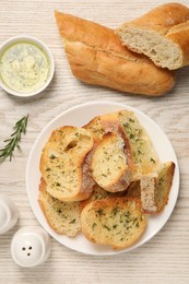 Tasty baguette with garlic served on white wooden table, flat lay