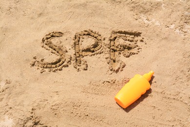 Photo of Abbreviation SPF written on sand and blank bottle of sunscreen at beach, above view