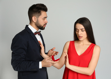 Photo of Young woman rejecting engagement ring from boyfriend on light grey background