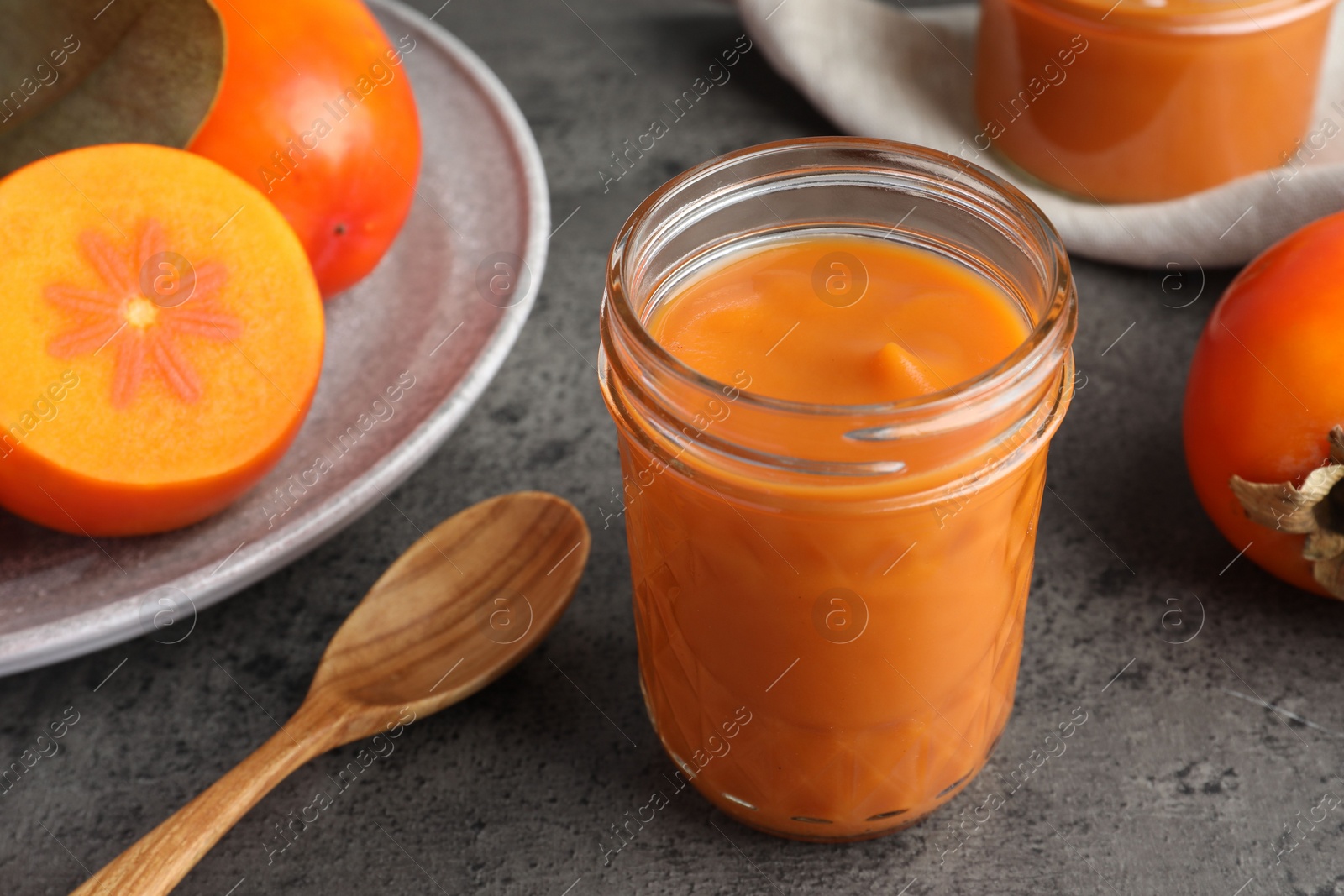 Photo of Delicious persimmon jam in glass jar served on gray table, closeup