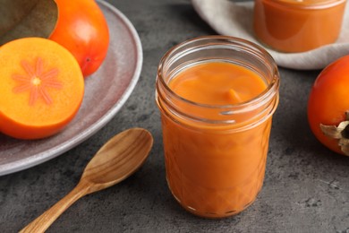 Delicious persimmon jam in glass jar served on gray table, closeup