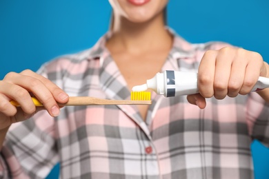Photo of Woman applying toothpaste on brush against blue background, closeup