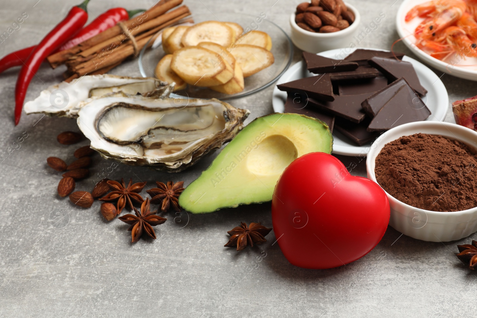 Photo of Natural aphrodisiac. Different food products and heart model on grey table, closeup