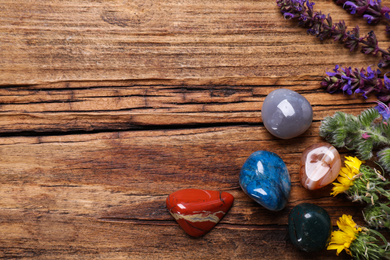 Flat lay composition with different gemstones and healing herbs on wooden table, space for text