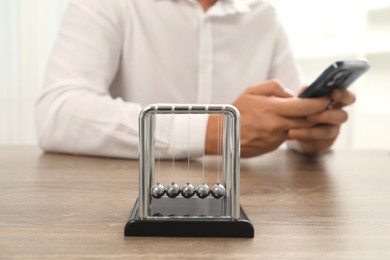 Photo of Newton's cradle and man using smartphone on wooden table, selective focus. Physics law of energy conservation