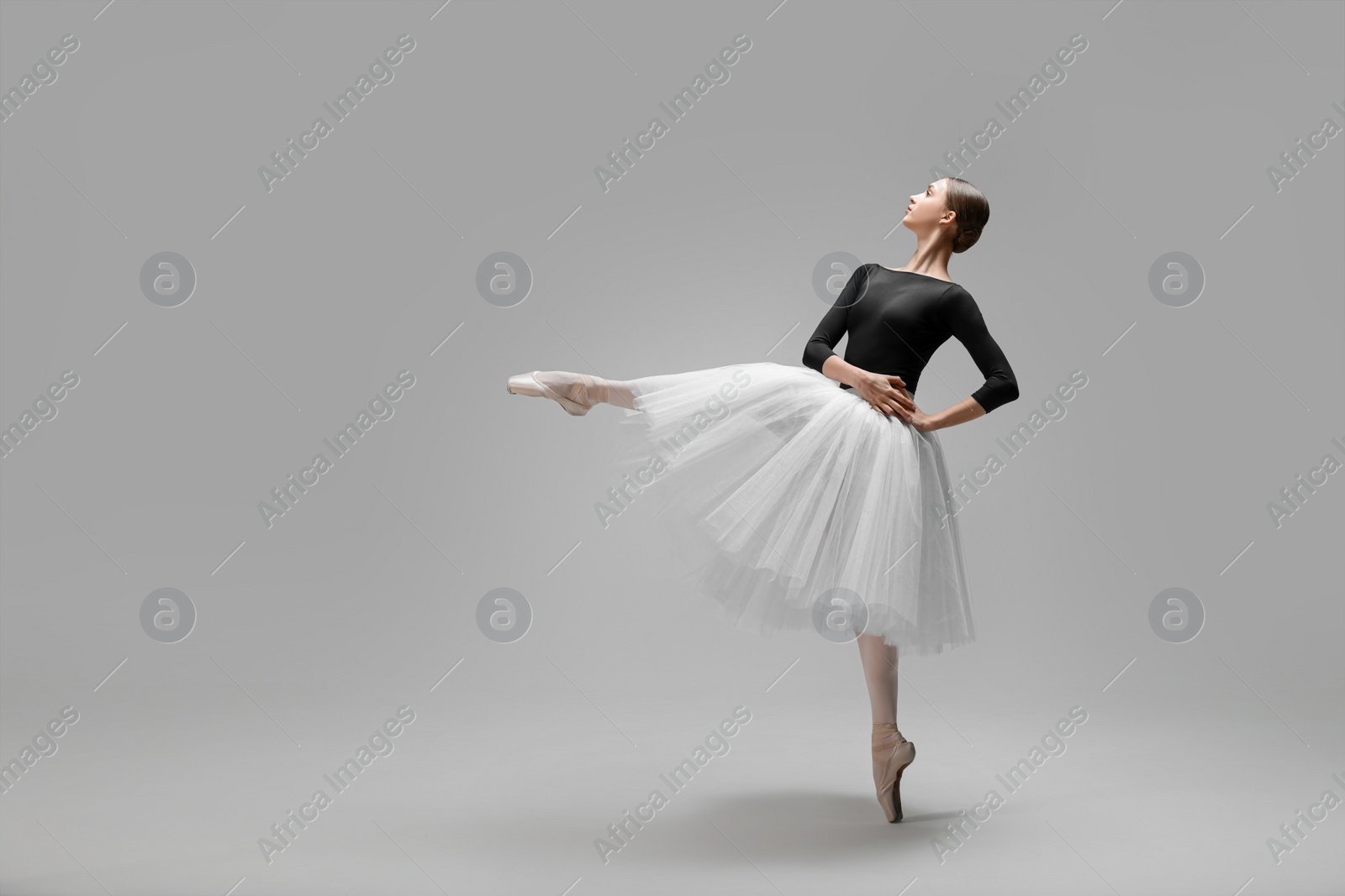 Photo of Young ballerina practicing dance moves on light grey background. Space for text