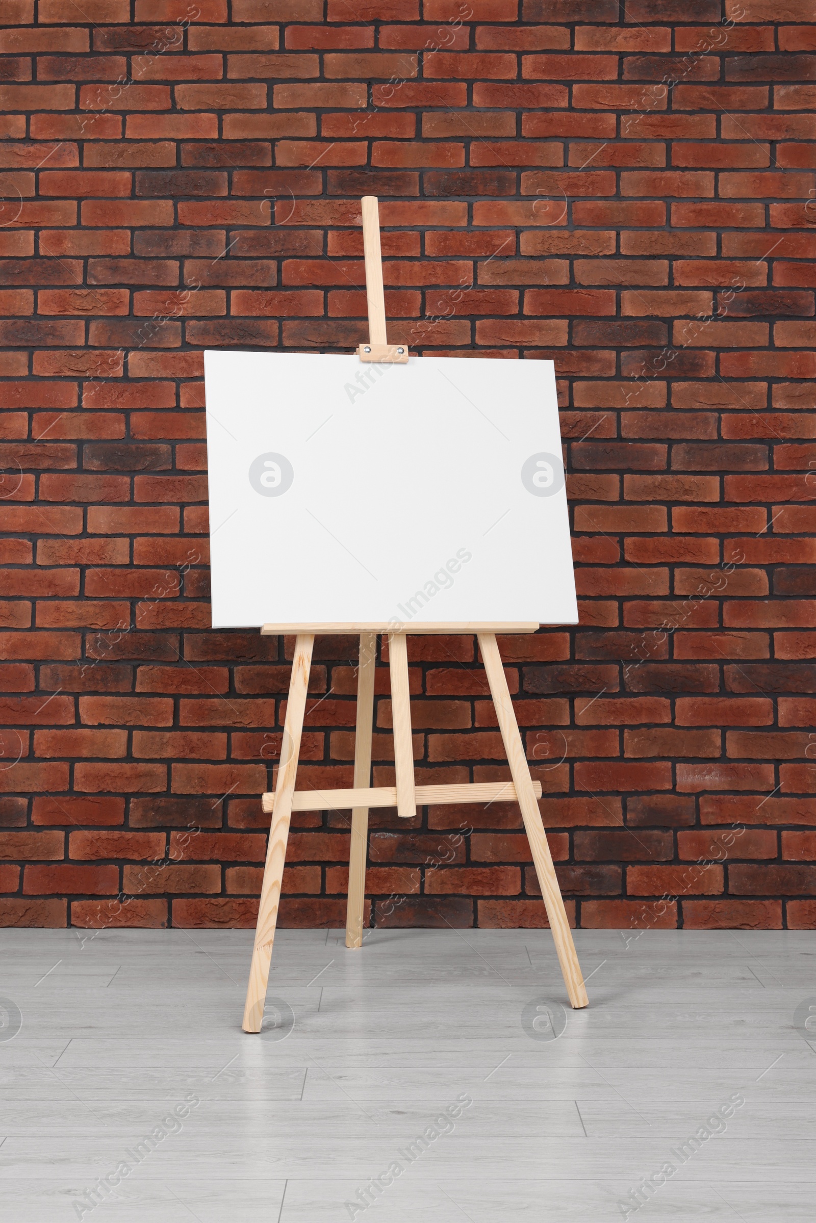 Photo of Wooden easel with blank canvas near brick wall indoors