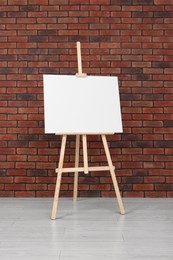 Photo of Wooden easel with blank canvas near brick wall indoors