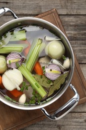 Different ingredients for cooking tasty bouillon in pot on wooden table, top view