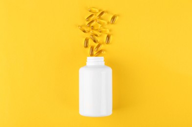 Photo of White medical bottle and vitamin capsules on yellow background, top view