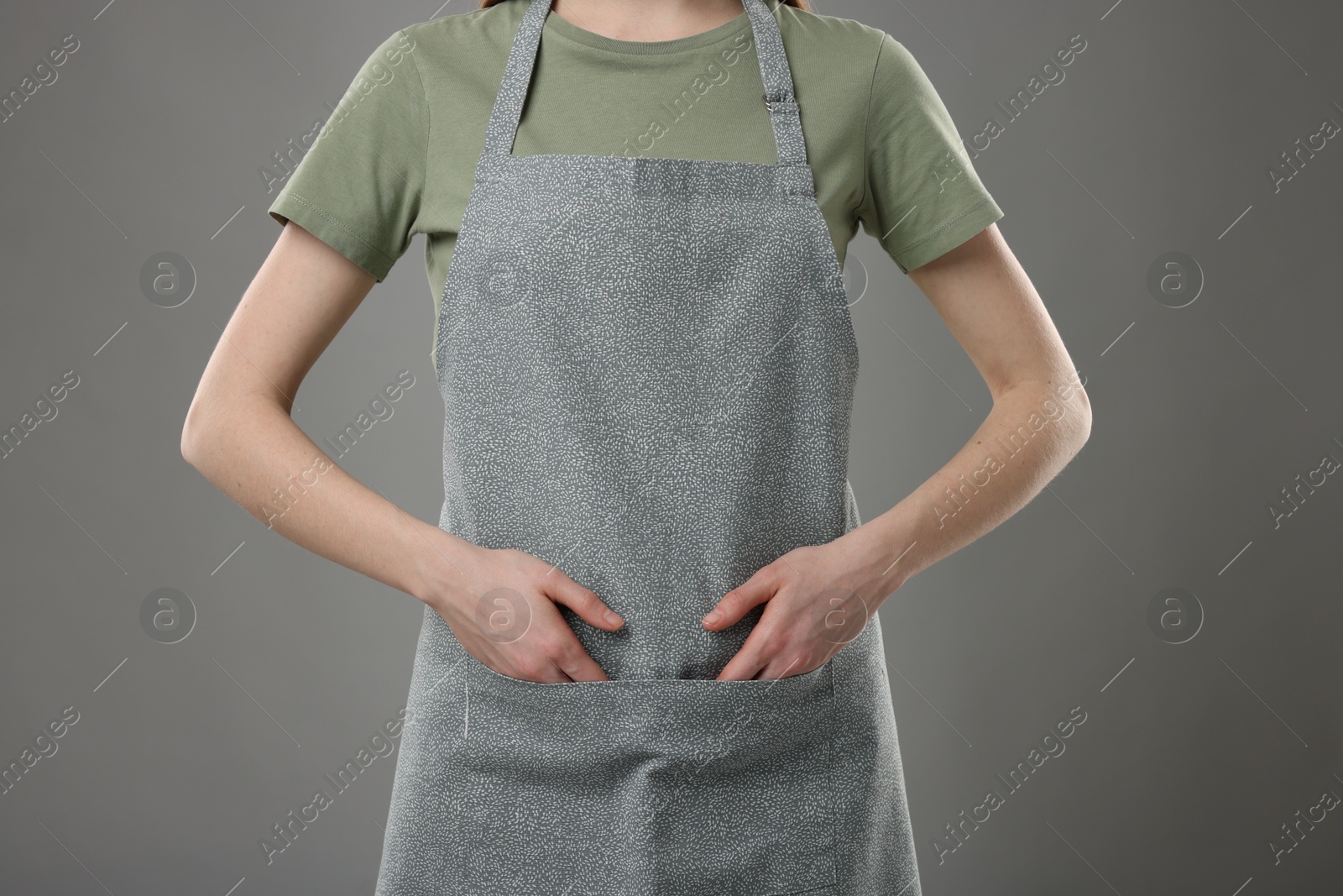 Photo of Woman wearing kitchen apron on grey background, closeup. Mockup for design