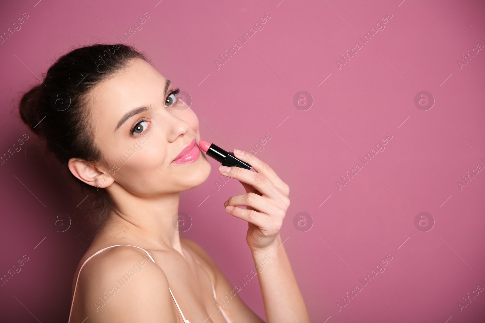 Photo of Young woman applying lipstick on color background. Professional makeup products