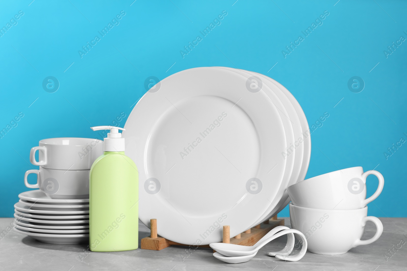 Photo of Set of clean tableware and dish detergent on grey table against light blue background