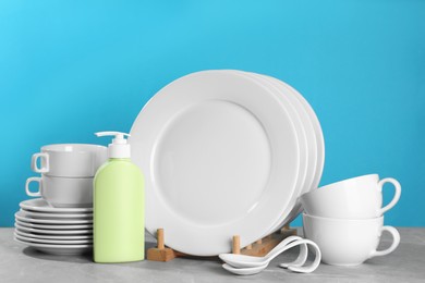 Set of clean tableware and dish detergent on grey table against light blue background