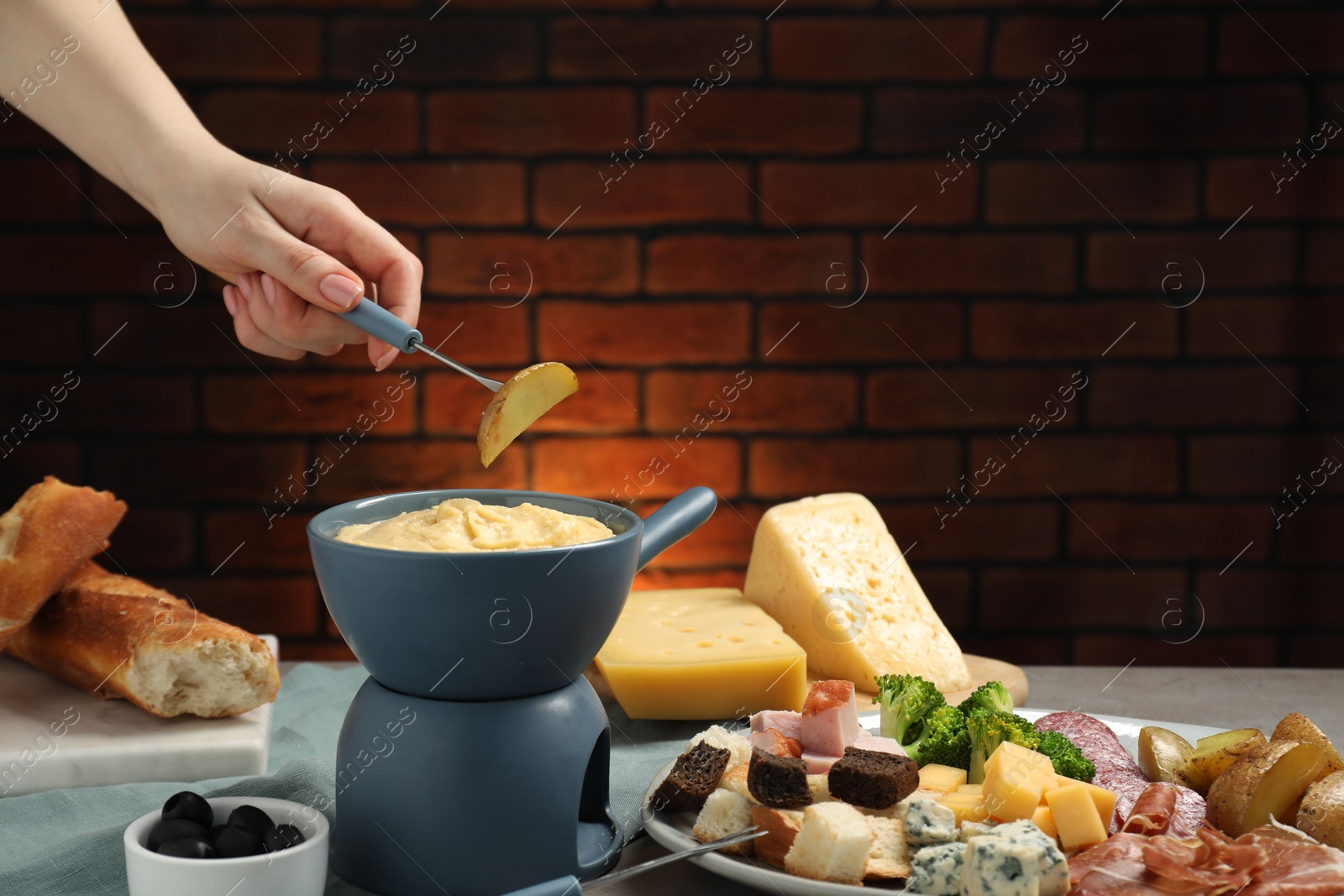 Photo of Woman dipping piece of potato into fondue pot with melted cheese at table with snacks, closeup. Space for text