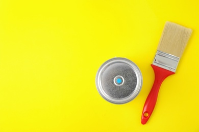 Photo of Closed can of paint with brush on yellow background, top view. Space for text