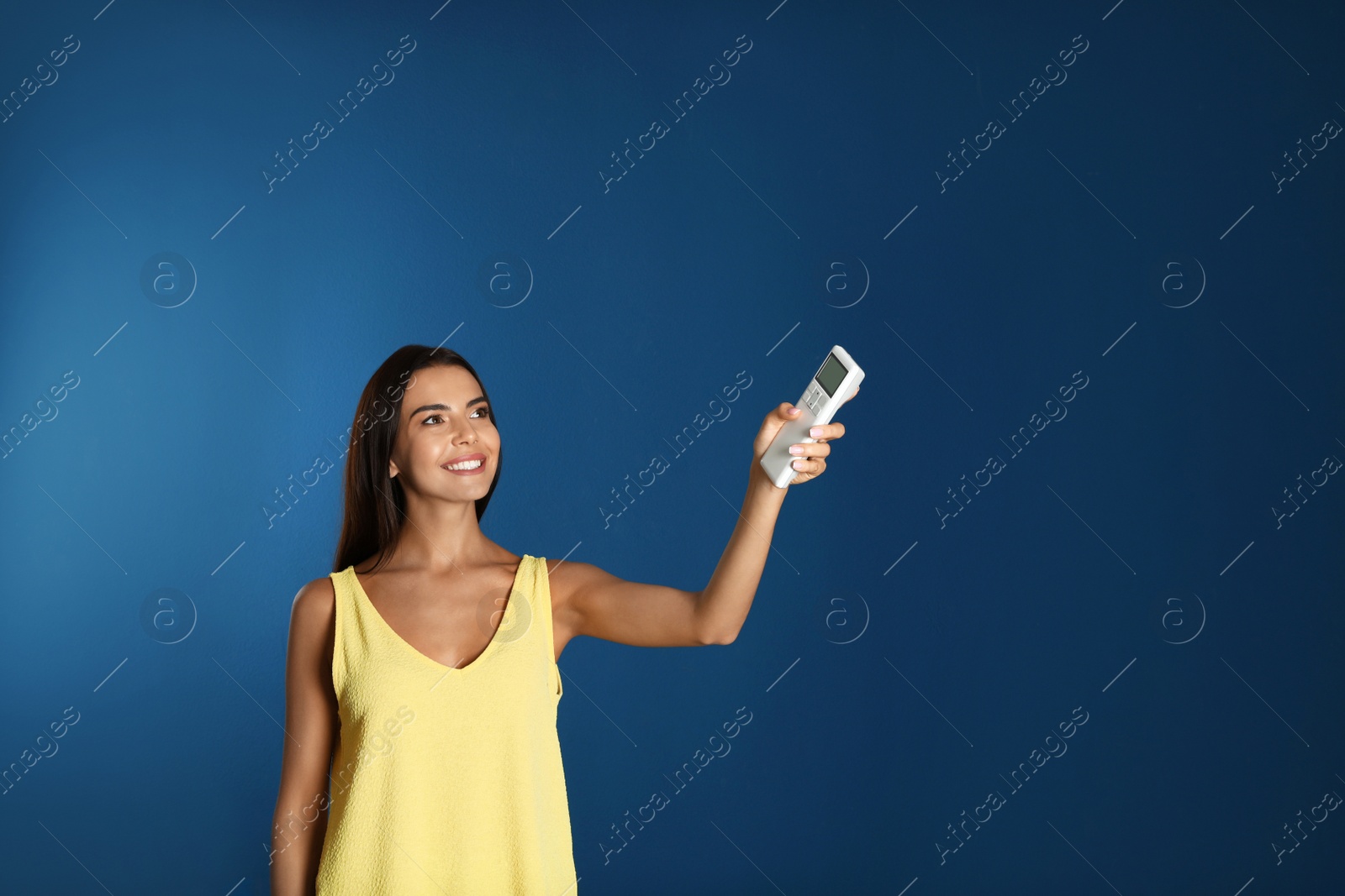 Photo of Young woman turning on air conditioner against blue background