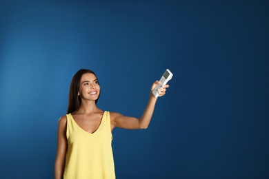 Photo of Young woman turning on air conditioner against blue background