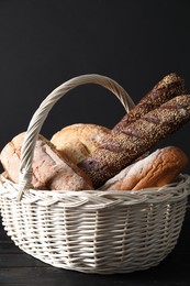 Photo of Wicker basket with different types of fresh bread on black table