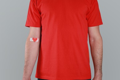 Blood donation concept. Man with adhesive plaster on arm against grey background, closeup