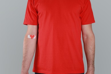 Photo of Blood donation concept. Man with adhesive plaster on arm against grey background, closeup