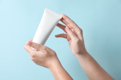 Photo of Woman with tube of hand cream on light blue background, closeup