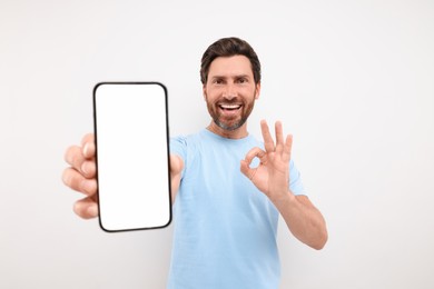 Photo of Handsome man showing smartphone in hand and OK gesture on white background