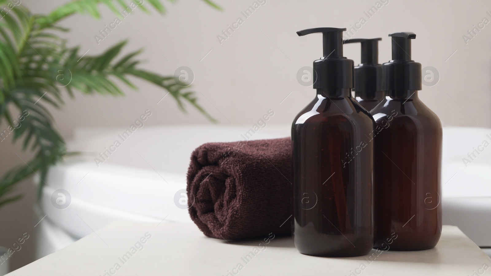 Bath foam and other personal hygiene products in bottles and rolled towel on small table in bathroom, space for text Photo of Bath foam and other personal hygiene products in bottles and rolled towel on small table in bathroom, space for text