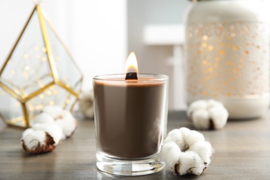 Photo of Burning candle and cotton flower on wooden table