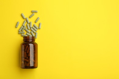 Vitamin pills and bottle on yellow background, top view. Space for text