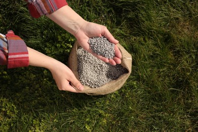 Photo of Woman with fertilizer on green grass outdoors, top view