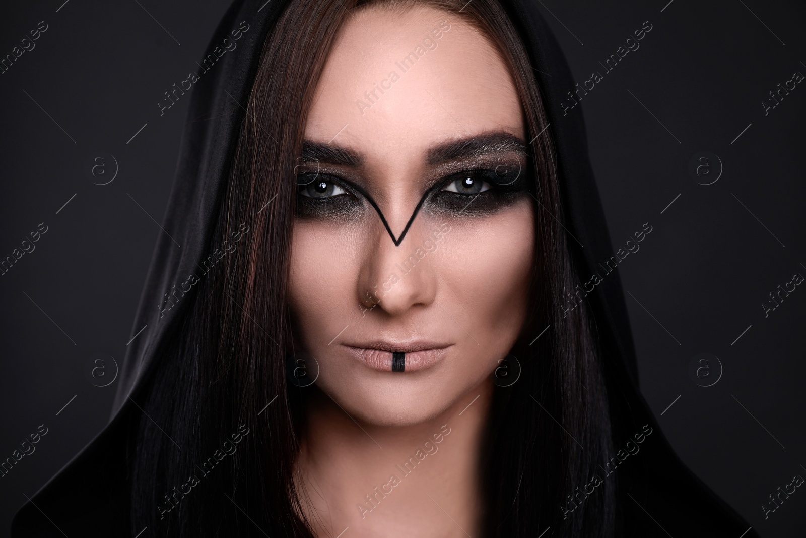 Photo of Mysterious witch in mantle with hood on black background, closeup